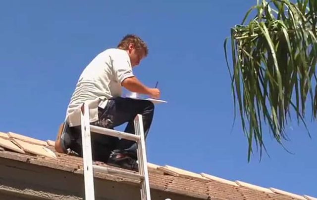 A KY-KO roofer kneels on top of a roof, taking details notes as part of our free roofing checkup.