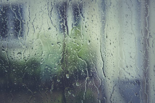 Rain falling onto glass window on a rainy day when the chance of a leaking roof is higher, with outside blurred.